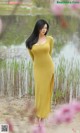 A woman in a yellow dress standing in front of a pond.