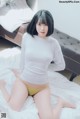 A woman in a white shirt and yellow panties sitting on a bed.