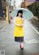 A woman in a yellow apron holding an umbrella.