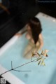 A woman in a bathtub with a branch in the water.