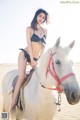 A woman in a bikini riding on the back of a white horse.