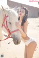 A woman in a white lingerie standing next to a white horse.