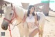 A woman in a white lingerie standing next to a white horse.