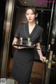 A woman in a black dress holding a tray with perfume bottles.