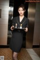 A woman in a black dress holding a tray with perfume bottles.