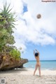 A naked woman throwing a hat in the air on a beach.