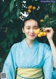 A woman in a blue and yellow kimono holding a bunch of fruit.