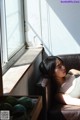 A woman laying on a brown leather couch next to a window.