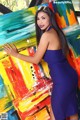 A woman in a blue dress posing in front of a painting.