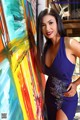 A woman in a blue dress leaning against a colorful painting.