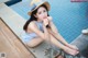 A woman sitting on the edge of a swimming pool wearing a straw hat.