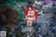 A woman in a red riding hoodie sitting on a rock in the woods.