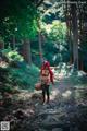 A woman in a red riding hoodie is walking through the woods.