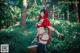 A woman in a red riding hoodie holding a basket in the woods.