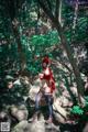 A woman in a red hoodie is posing on a rock in the woods.