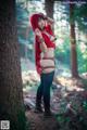 A woman in a red hooded outfit standing next to a tree.