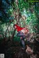 A woman in a red riding hoodie is posing in the woods.