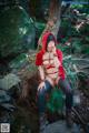 A woman in a red hooded outfit sitting on a rock in the woods.