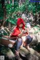 A woman in a red hooded outfit sitting on a rock with a basket.