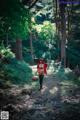 A woman in a red riding hoodie is walking through the woods.