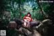 A woman in a red riding hoodie sitting on a rock in the woods.