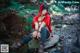 A woman in a red hoodie sitting on a rock in the woods.