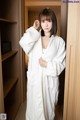 A woman in a white robe standing in a closet.