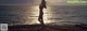 A woman standing on a rock by the ocean at sunset.