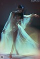 A woman in a white dress is dancing in the dark.