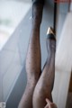 A woman wearing black stockings and high heels leaning against a window.