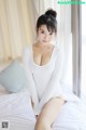 A woman in a white bodysuit sitting on a bed.