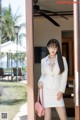 A woman in a white suit and glasses standing in front of a door.