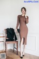 A woman in a brown dress standing next to a chair.