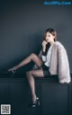 A woman sitting on top of a black cabinet with her legs crossed.