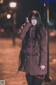 A woman in a brown coat standing on a street at night.