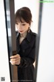 a woman in a black trench coat looking at herself in the mirror