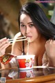 A woman eating a bowl of noodles with chopsticks.