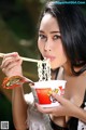 A woman eating a bowl of noodles with chopsticks.