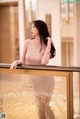 A woman in a pink dress leaning on a railing.