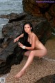 A naked woman sitting on a rock by the ocean.