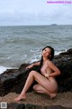 A naked woman sitting on a rock by the ocean.