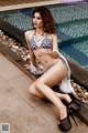 A woman in a bikini sitting by a swimming pool.