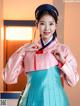 A woman in a pink and blue hanbok poses for a picture.