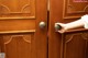 A person is opening a wooden door with a brass door knob.