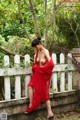 A woman in a red dress is posing on a fence.