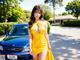 A woman in a yellow dress standing next to a blue car.