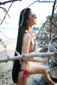 A woman in a bikini sitting on a rock on the beach.