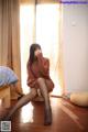 A woman sitting on a bed in a room with a window.