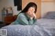 A woman sitting on a bed with her hand on her chin.