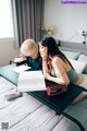 A man and a woman sitting on a bed looking at a book.